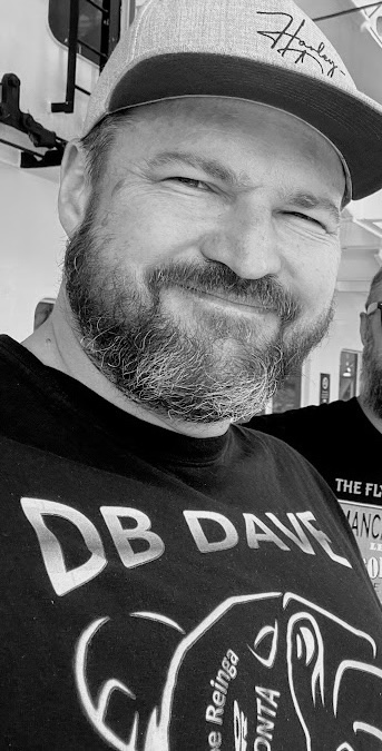 A black-and-white selfie of me, bearded and grinning in a cap and a &ldquo;DB DAVE&rdquo; t-shirt.