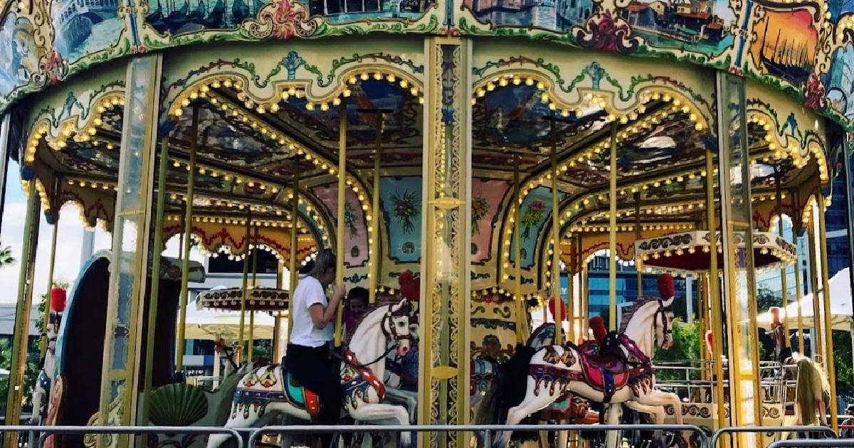 An ornate carousel spinning in the sunshine, with an EXIT sign on the railing in the foreground
