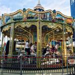 An ornate carousel spinning in the sunshine, with an EXIT sign on the railing in the foreground